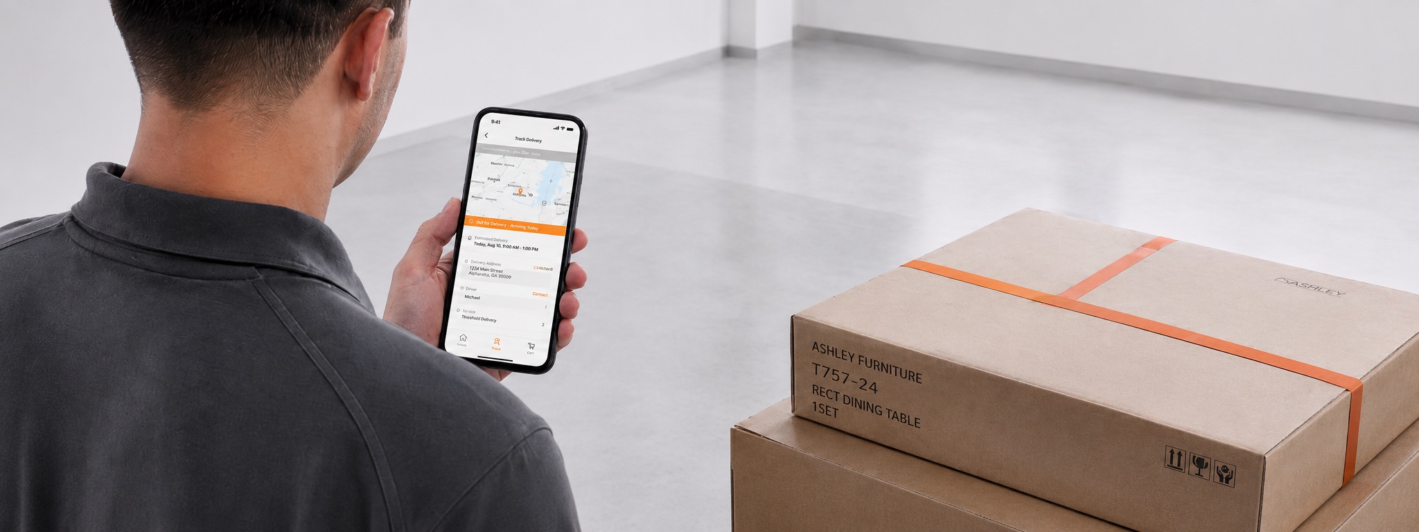 Employee tracking a delivery on the TNT app beside stacked Ashley cartons